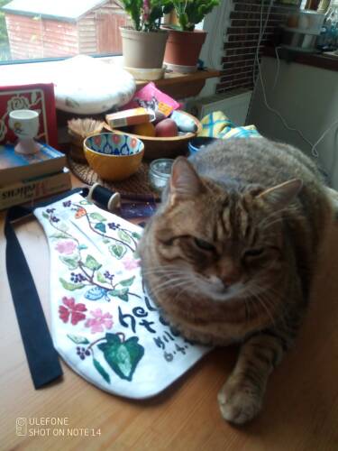 A  tabby cat sits on an embroidered Pocket in the midst of sewing materials